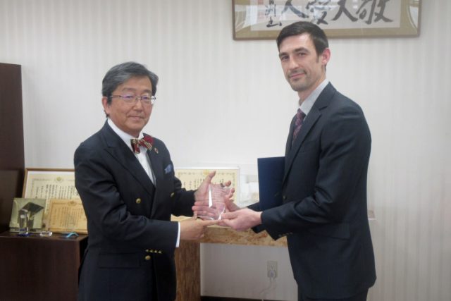 岡山大学長から受賞の楯を受け取るライアン准教授のようす