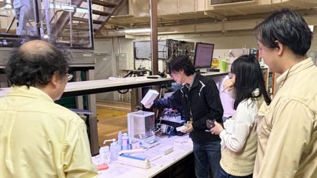 科学分析の方法について説明を行う男性とそれを聞く複数の人々