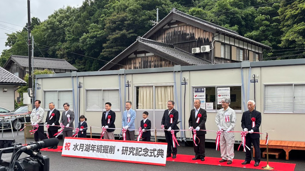 建物の前に人が並びテープカットをするようす
人々の前には「祝 水月湖年縞掘削・研究記念式典」と書かれた看板がある