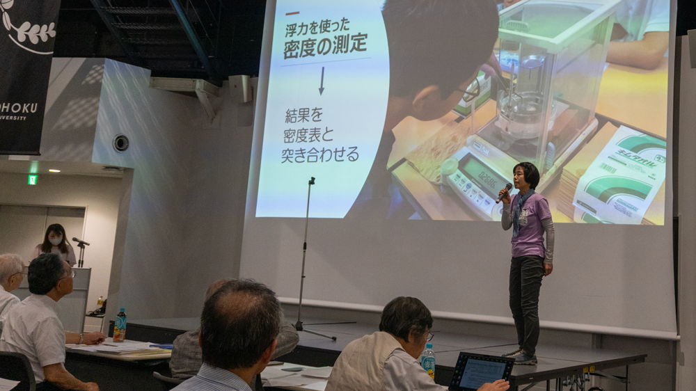 壇上でマイクをもって話す人とスライドを操作する人