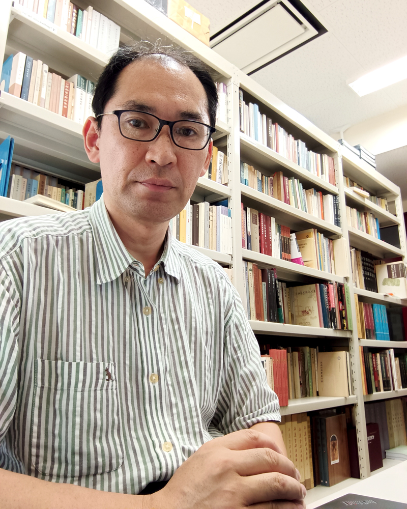 本棚を背にして座る男性