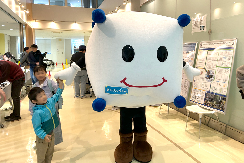 着ぐるみのマスコット「きんけんちゃん」が子どもたちと手を繋いでいるようす