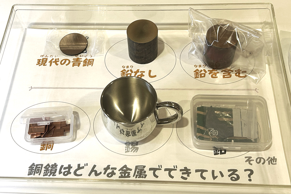 円柱状の青銅2種と青銅の原料（銅・錫・鉛）を並べた展示「銅鏡はどんな金属でできている？」
