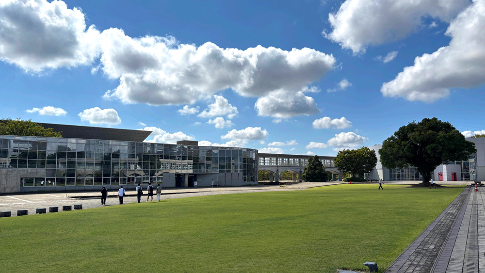 緑の芝生と青い空、白い雲の間にガラス張りの建物が見える風景
