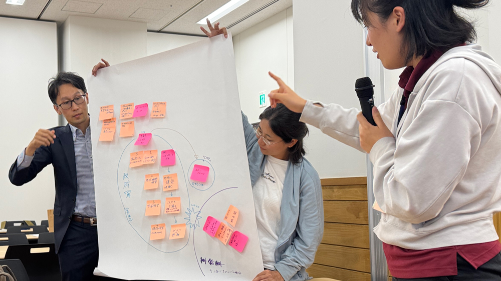 ポスターを掲げ持つ人と、それを指さし説明する女性