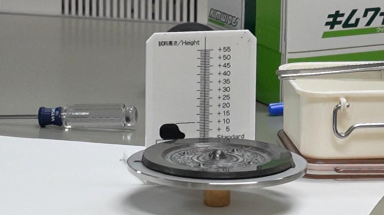 円形の台に載せられた銅鏡と、試料の高さを測る定規