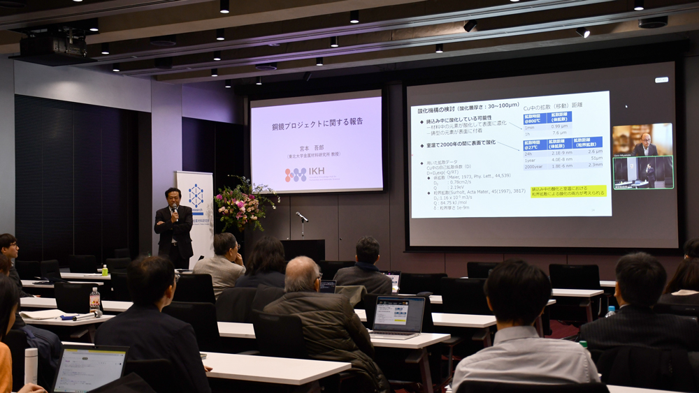 オンライン発表でスライド画面に映る登壇者とそれを見つめる会場の参加者