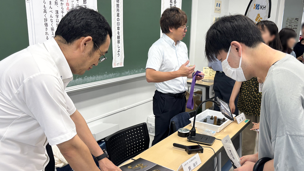 教室の机の上に置かれた本を見ながら話している人々と、説明している人