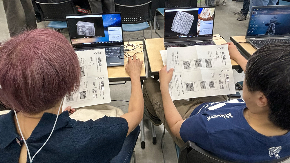 プリントを広げてノートパソコンの画面と見比べる人々