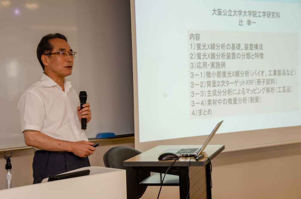 スクリーンの横でマイクを持って話している男性